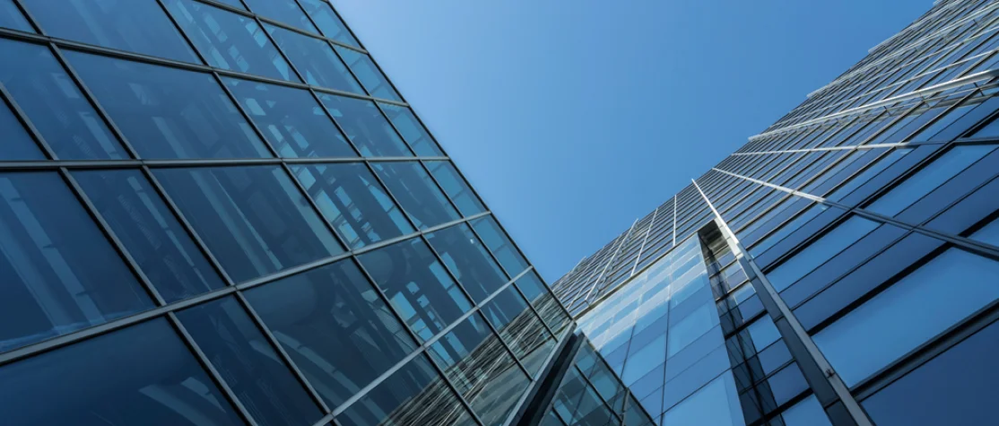 Low-angle view of modern glass office buildings reflecting the blue sky, showcasing sleek architectural lines and a clean, reflective facade.