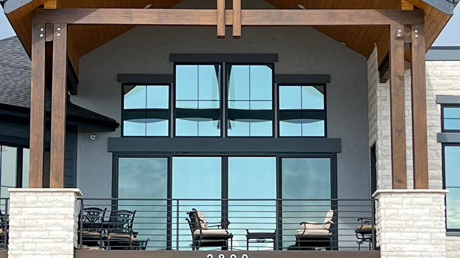 Large modern home with tall, reflective windows and a covered patio featuring outdoor seating and wooden beams.