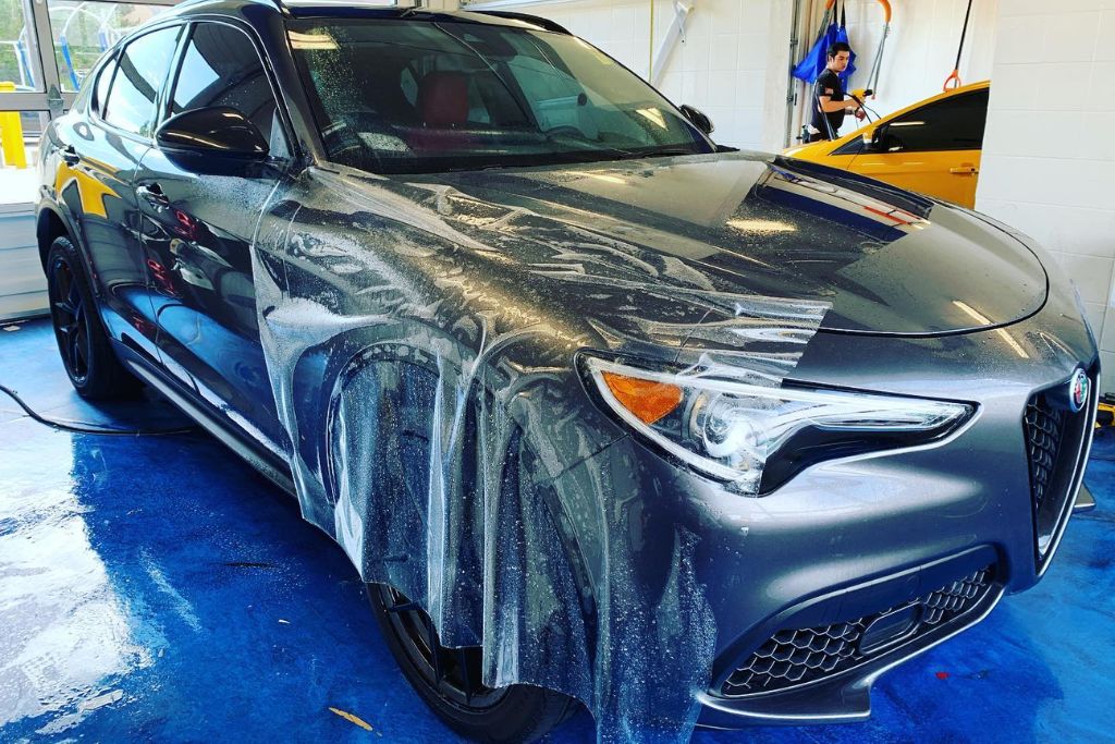 A dark gray Alfa Romeo SUV undergoing partial paint protection film installation in a detailing bay, with the film visibly draped and aligned over the front fender and hood. The soapy application process highlights the precision involved in PPF coverage in Douglas County, USA.
