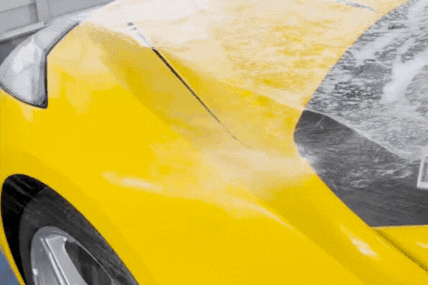 Close-up of a yellow car’s hood during the paint protection film installation process, showing a technician smoothing the clear film over soapy surface to bond it seamlessly. This step highlights the precision and clarity of modern PPF technology used in Douglas County, USA.