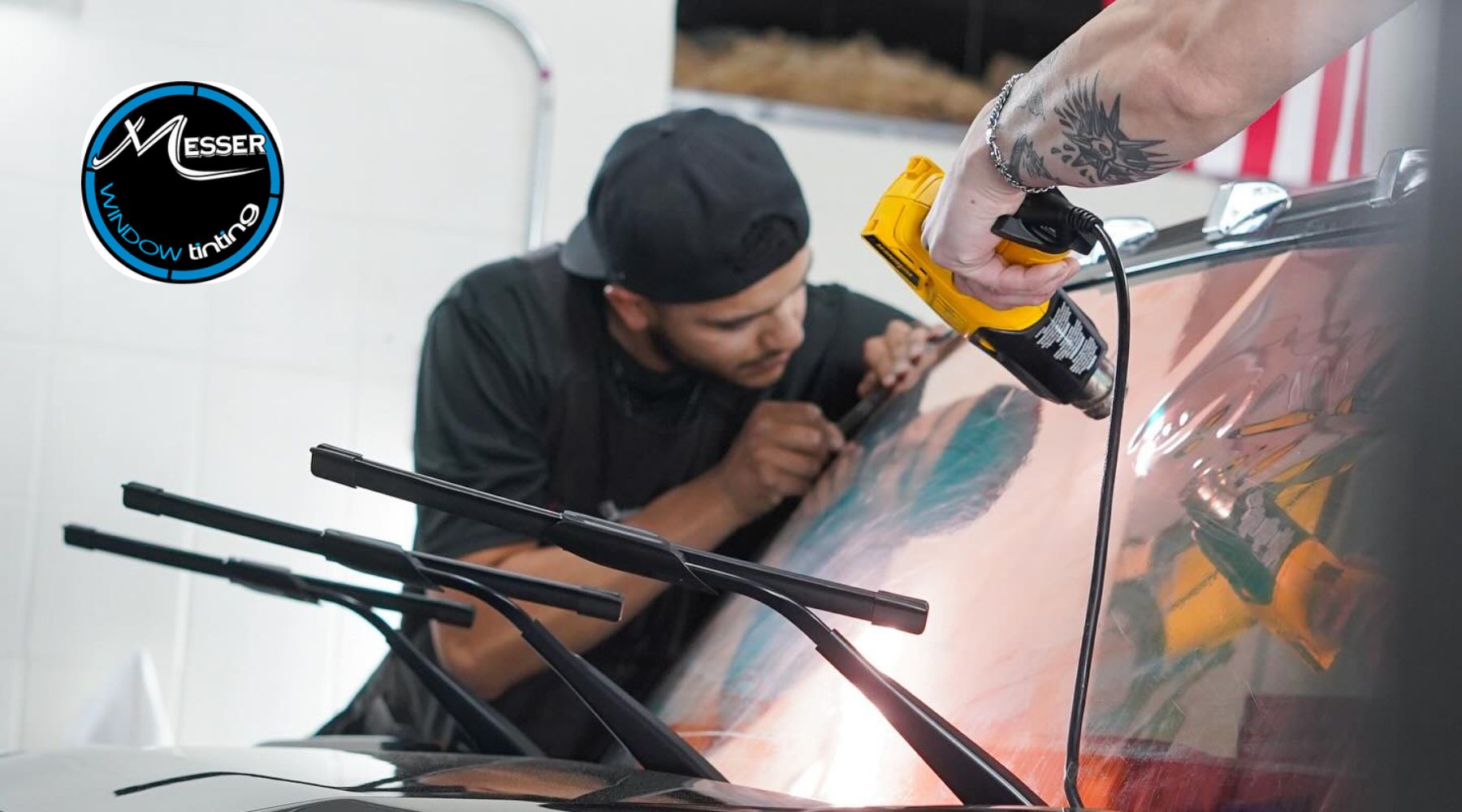 A technician in Colorado applies a heat gun while carefully installing a window tint film on a vehicle windshield, showcasing the precision involved in professional tinting. This hands-on process illustrates what is window tinting and how it benefits Colorado drivers by reducing glare and improving year-round comfort.