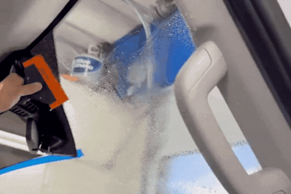 Interior view of a car as a technician uses a squeegee to smooth out window tint film on the front windshield, with water and application solution visibly sprayed. This installation step clearly demonstrates what is window tinting by showing how the film is carefully applied to improve UV protection and visibility in Colorado driving conditions.