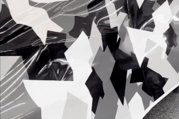 Close-up GIF of a black, white, and gray geometric camouflage vinyl wrap being smoothed onto a vehicle panel, demonstrating the hands-on process involved in Understanding Vinyl Wrapping.
