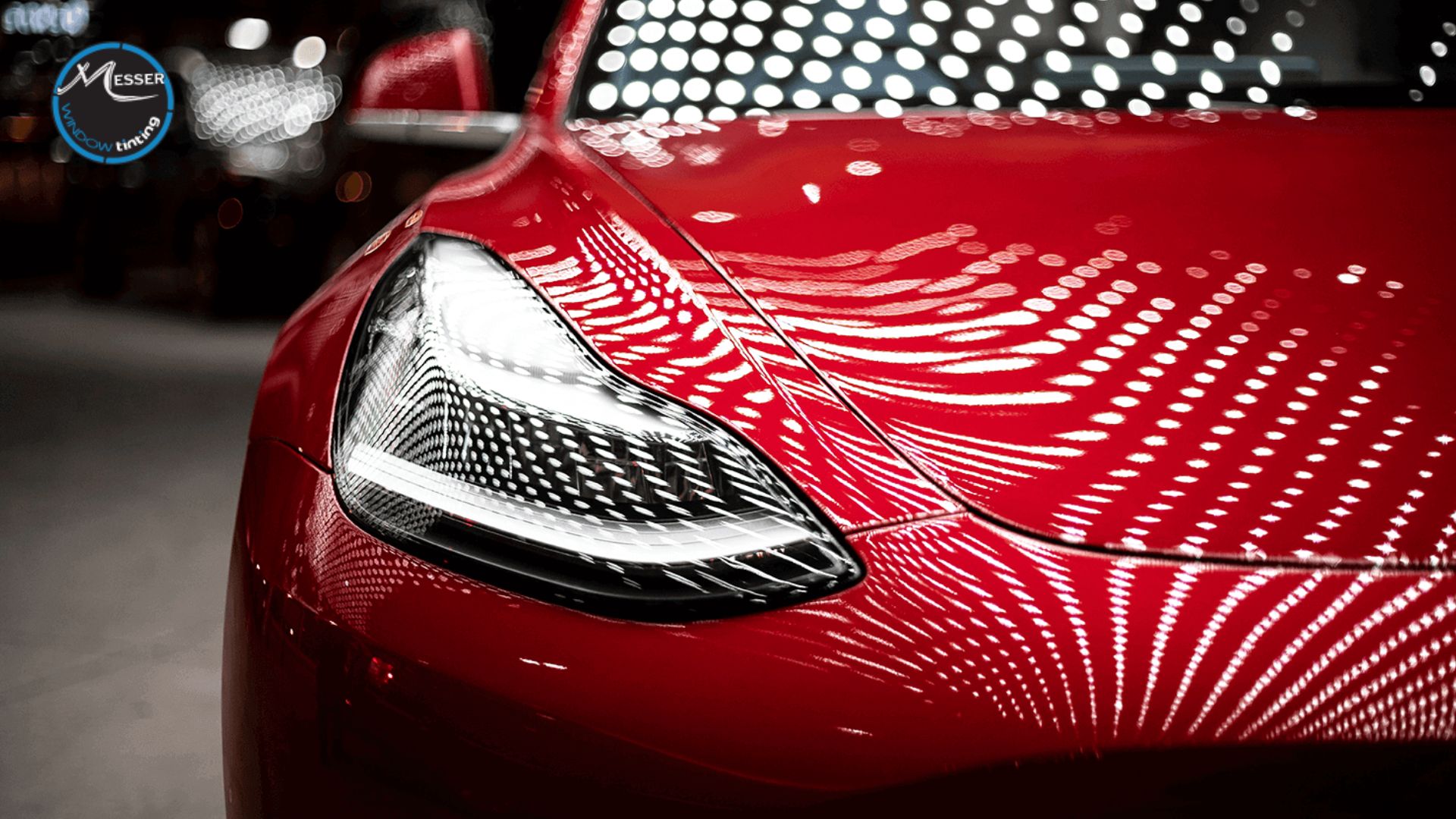 Close-up of a red car's headlight and hood under bright studio lights, with dramatic reflections showcasing the deep gloss and mirror-like finish achieved by ceramic coating.