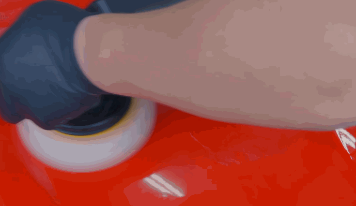 Hand polishing a red car panel with a dual-action buffer to remove imperfections before ceramic coating application.