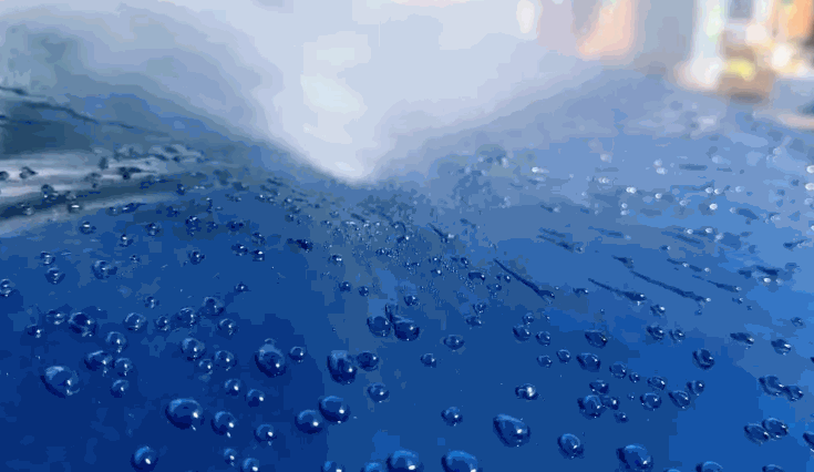 Close-up of water beading and rolling off a blue car surface after ceramic coating, showing high hydrophobic properties.