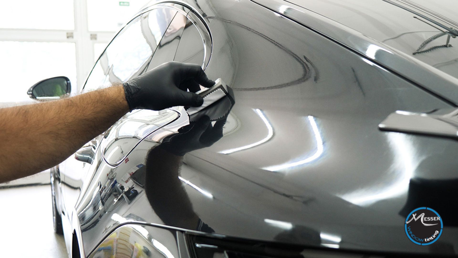 Close-up of a person in black gloves applying ceramic coating to the side of a glossy black car using a microfiber-wrapped applicator.