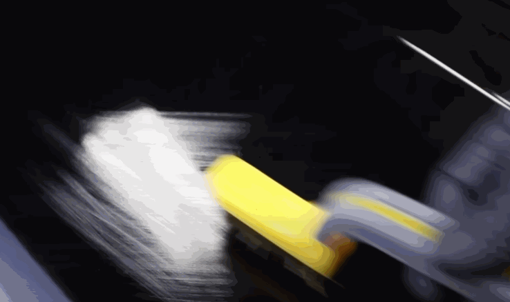 A gloved hand uses a yellow squeegee to press down a white vinyl wrap on a glossy black car surface.