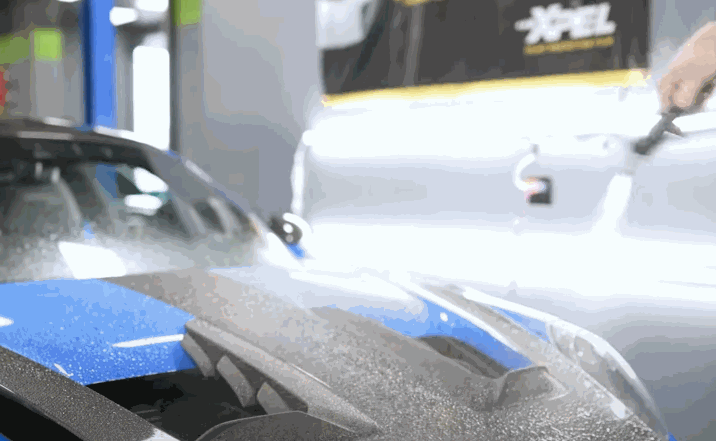 Close-up of a car hood being sprayed with solution during a paint protection film installation.