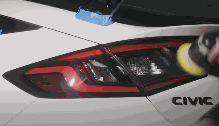 Detailer polishing the rear tail light of a white Honda Civic using a machine polisher to enhance gloss and protection. The process prepares the surface for ceramic coating or wax to improve shine and durability.