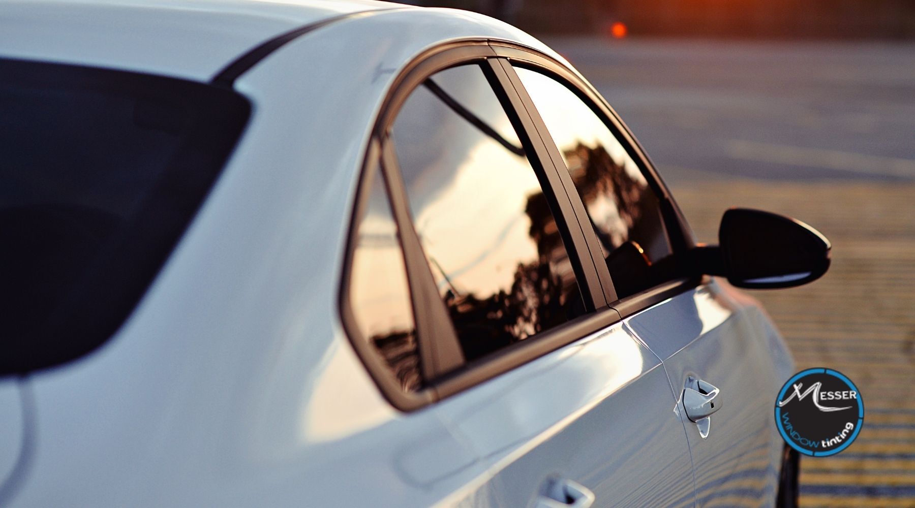 White sedan with dark window tint parked outdoors at sunset, showcasing side windows and rear passenger glass.