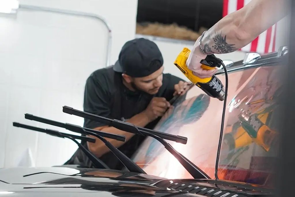 Technician using a heat gun to install automotive window tint on a car windshield at Messer Window Tinting.