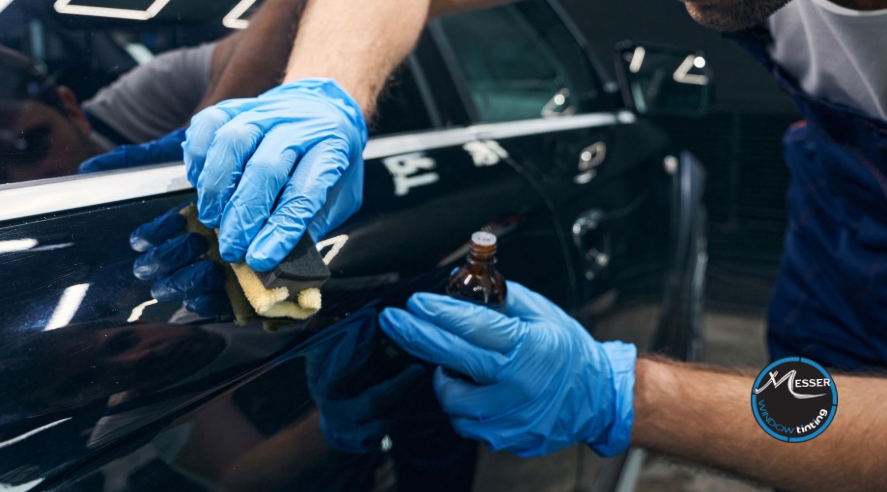 Technician applying ceramic coating to a black car door with a foam applicator while holding a small bottle of product.