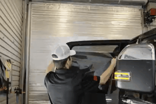 Technician installing window tint film on a vehicle window inside the Messer Window Tinting workshop.