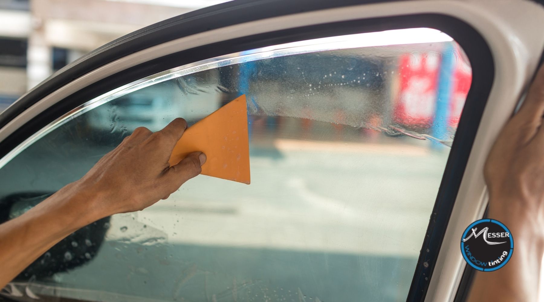 Technician applying window tint film to a car door window using an orange squeegee at Messer Window Tinting