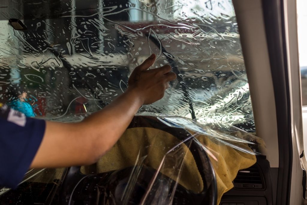 Technician applying window tint film to a vehicle windshield during professional installation at Messer Window Tinting