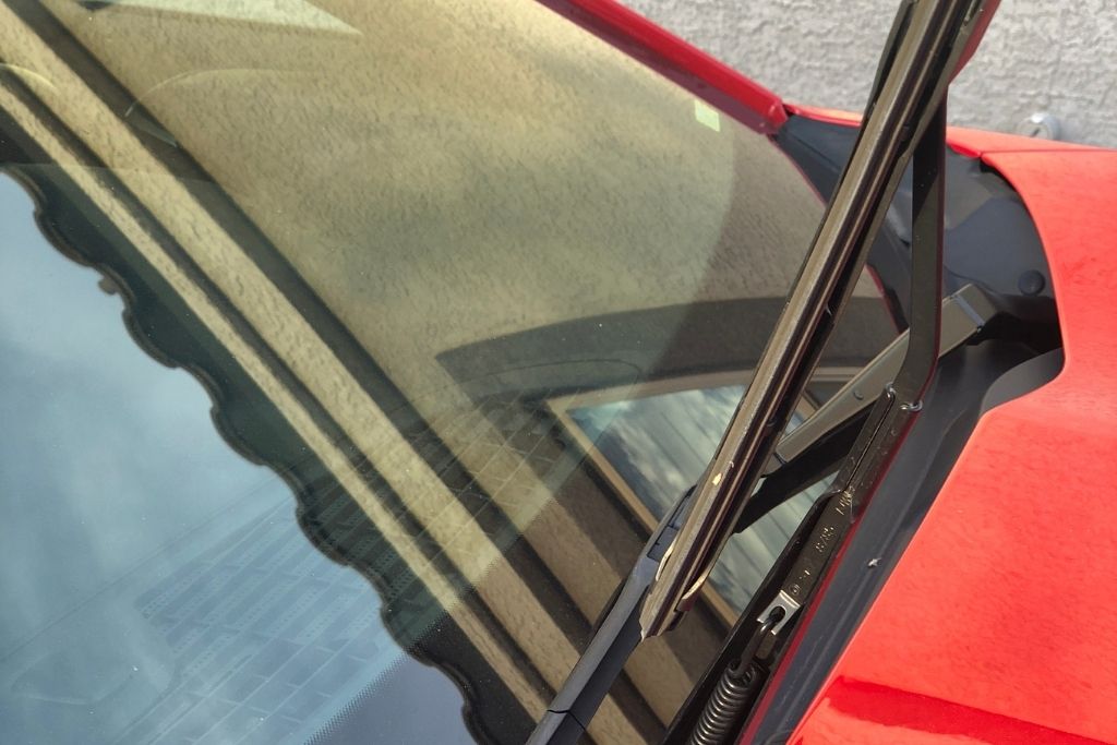 Close-up of a tinted car windshield with the wiper raised on a red vehicle
