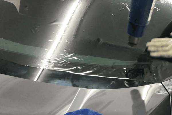 Heat shrinking window tint film onto a car windshield during professional installation